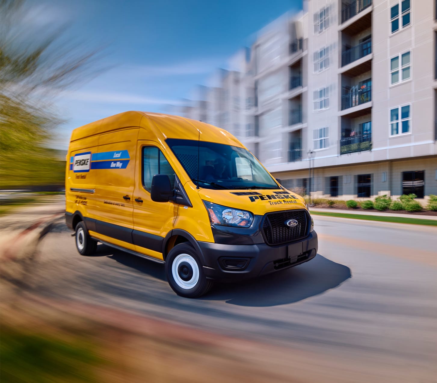 Yellow Penske rental truck driving down city street.